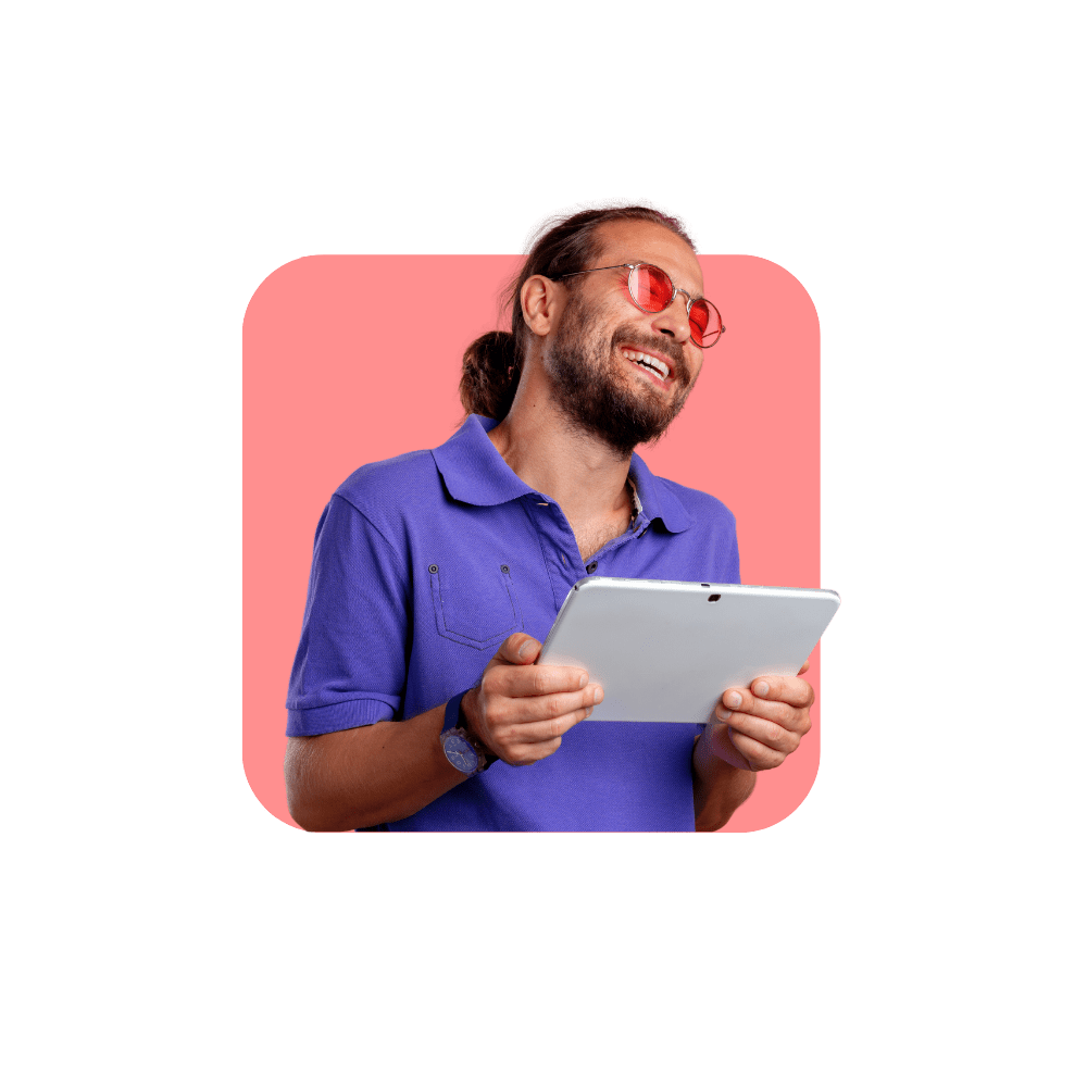 Homme qui sourit avec tee-shirt violet et lunettes roses avec une tablette à la main sur fond rose