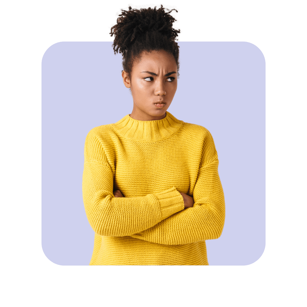 Femme métisse pull jaune bras croisés sourcils froncés sur fond violet clair