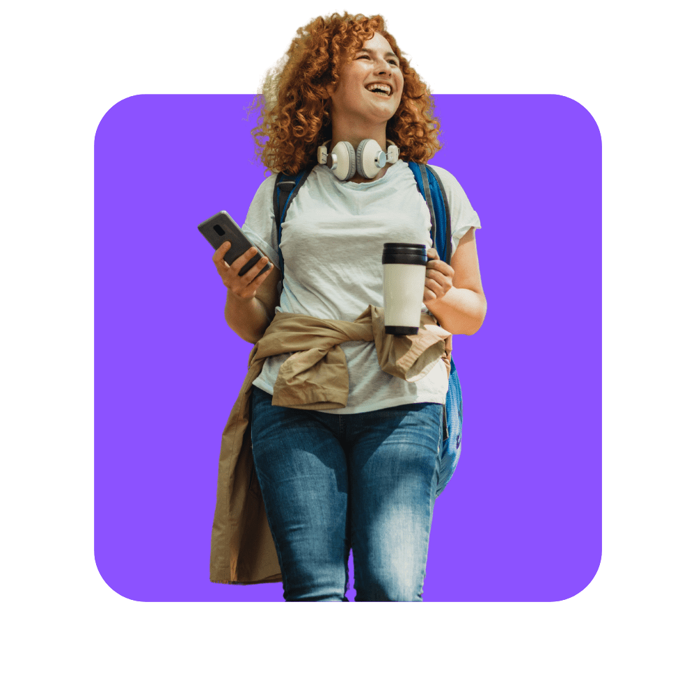 femme avec tee shirt blanc, jean et trench beige autour de la taille, téléphone dans une main et café dans l'autre.