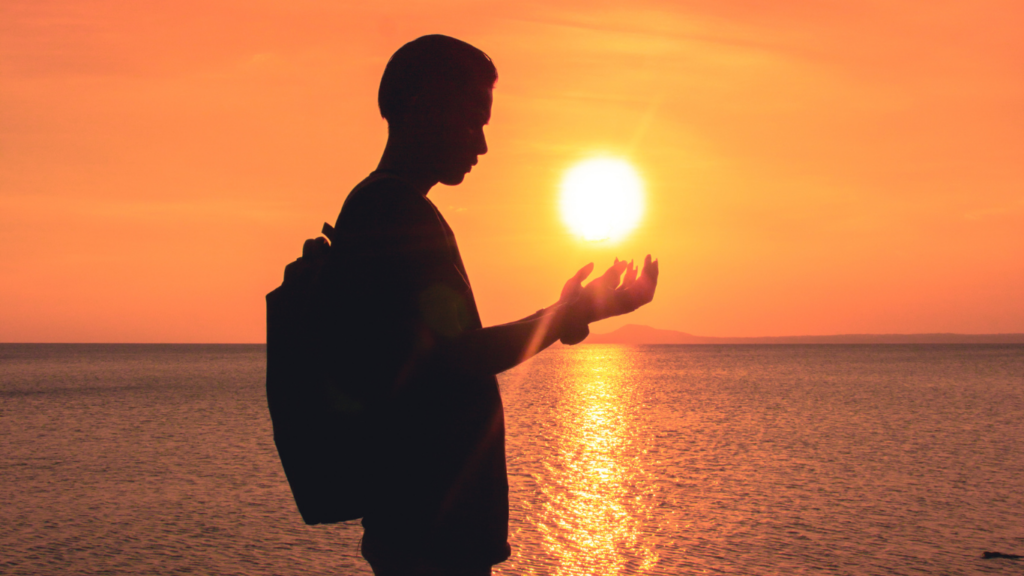Ombre d'un homme avec sac à dos tenant dans ses mains le soleil avec la mer en fond