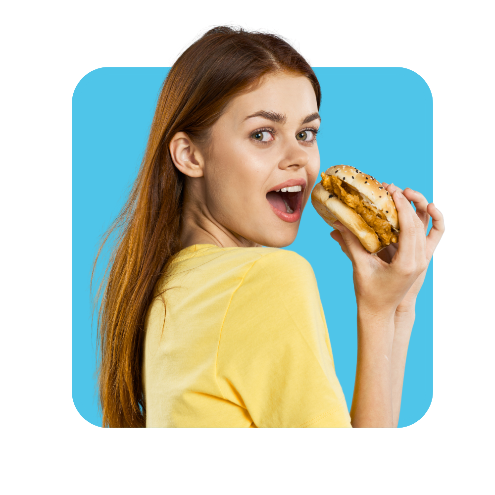 Femme avec tee shirt jaune sur fond bleu qui va manger un hamburger.
