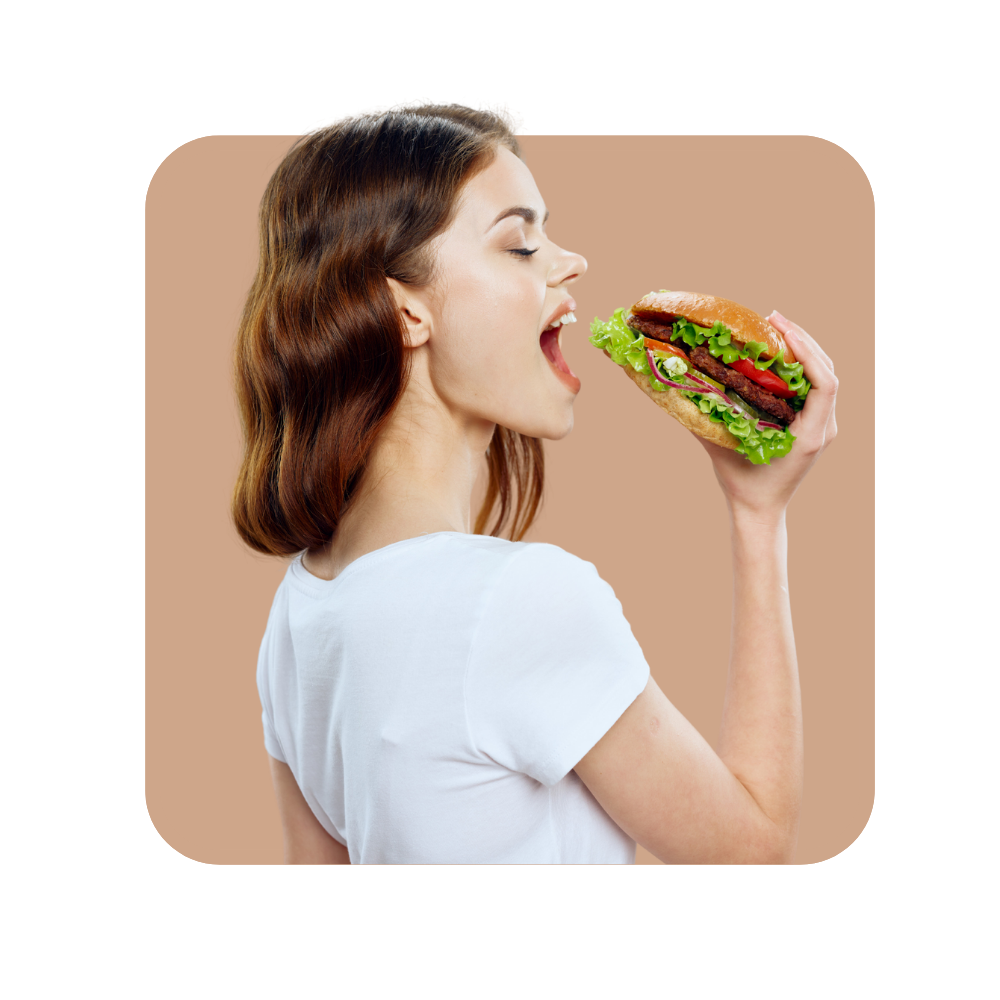 Femme avec tee shirt blanc sur fond ocre en train de croquer dans un hamburger - formation à la vente additionnelle