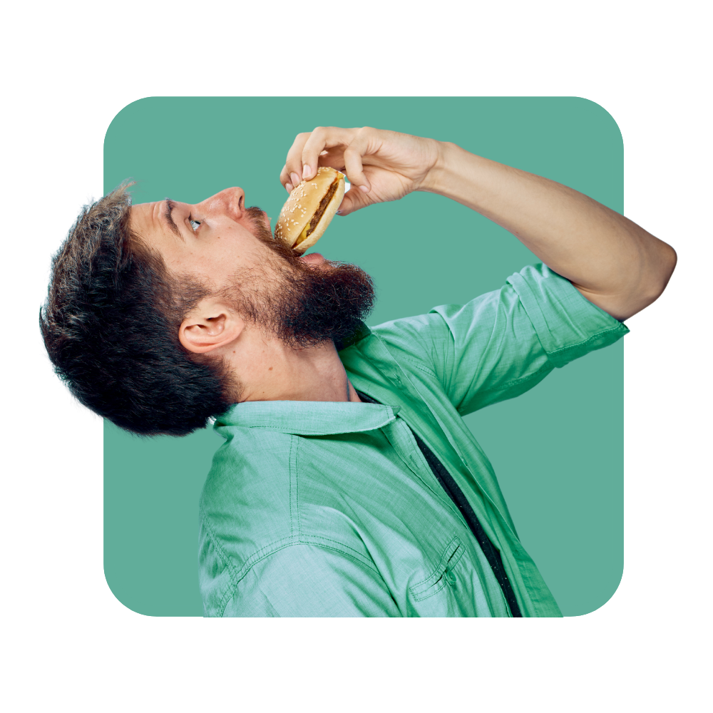 homme avec chemise verte penché mettant un hamburger dans sa bouche sur fond vert -